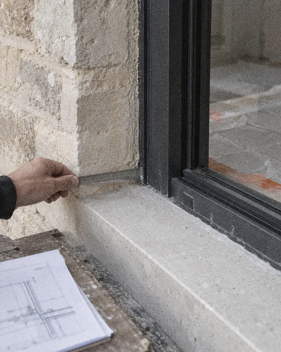 Contrôle au réglet du raccord entre la pierre et une menuiserie noire, sur le chantier