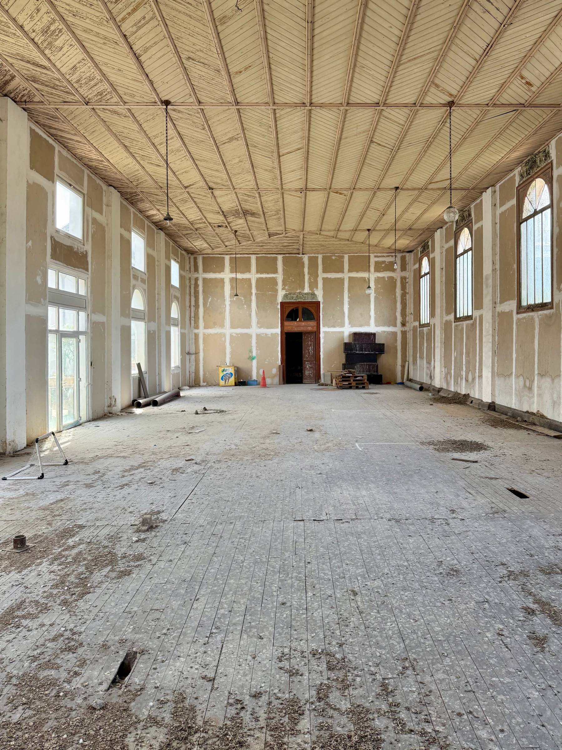 Vue en enfilade de la salle vide avant réhabilitation, charpente et lanterneaux latéraux, sol en attente de travaux