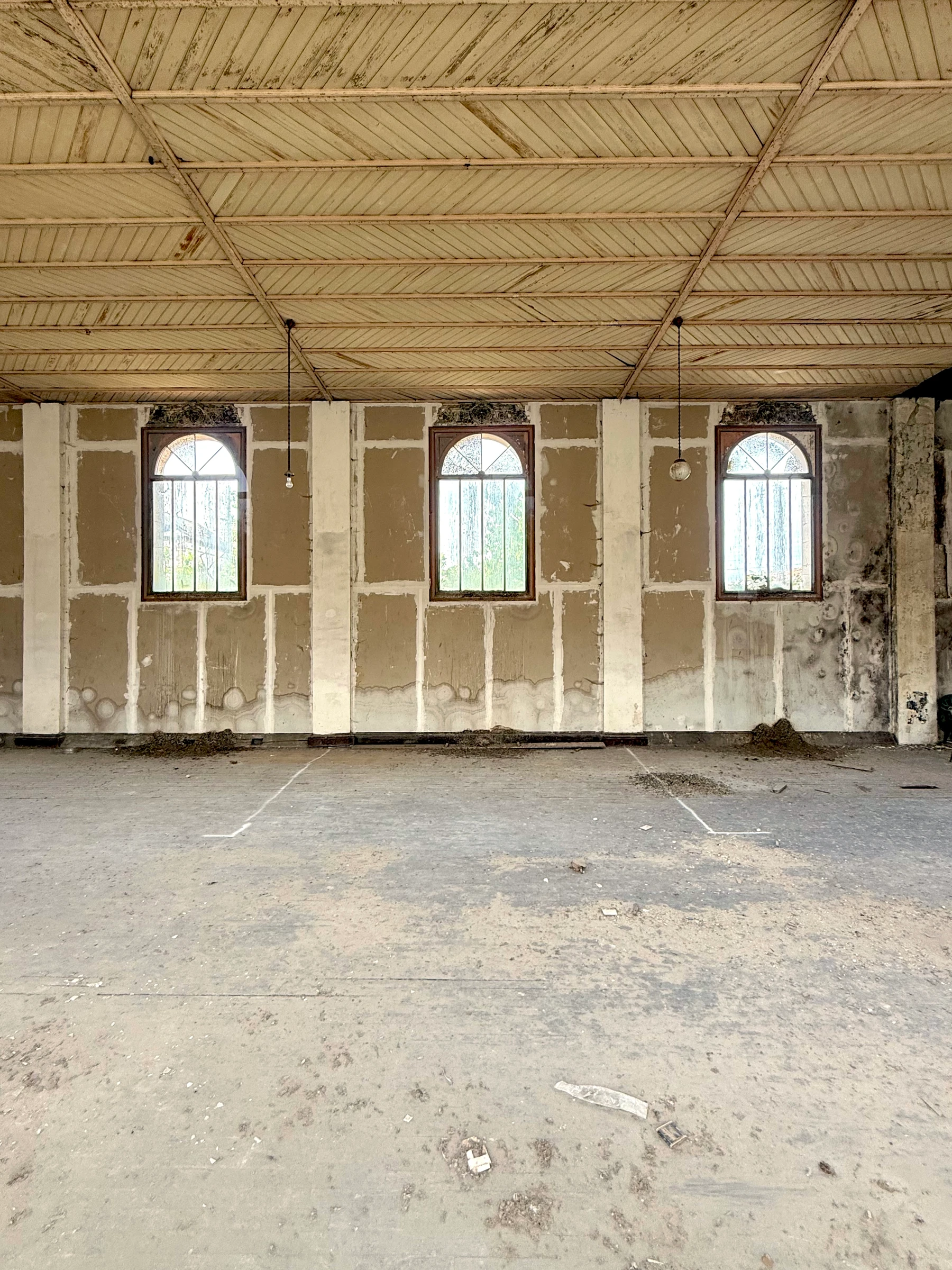 Vue d'ensemble de l'ancienne salle avant travaux, trois fenêtres en arc plein cintre et charpente bois apparente