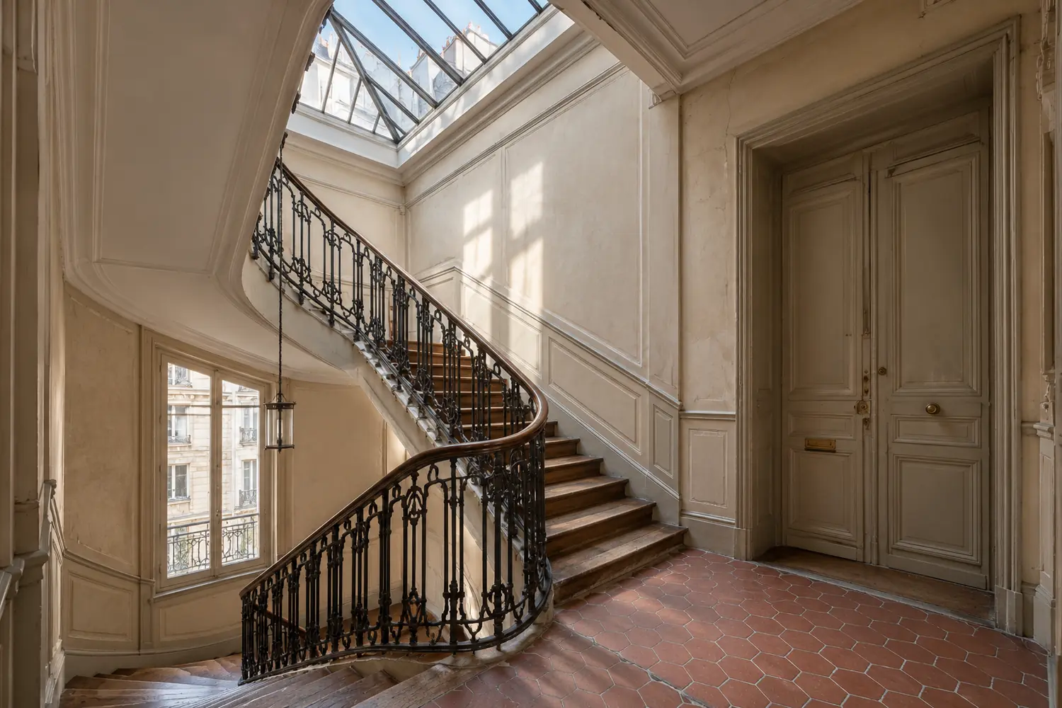 Cage d’escalier d’un immeuble parisien ancien, rampe en fer forgé et tomettes, vue depuis le palier lors d’une contre-visite