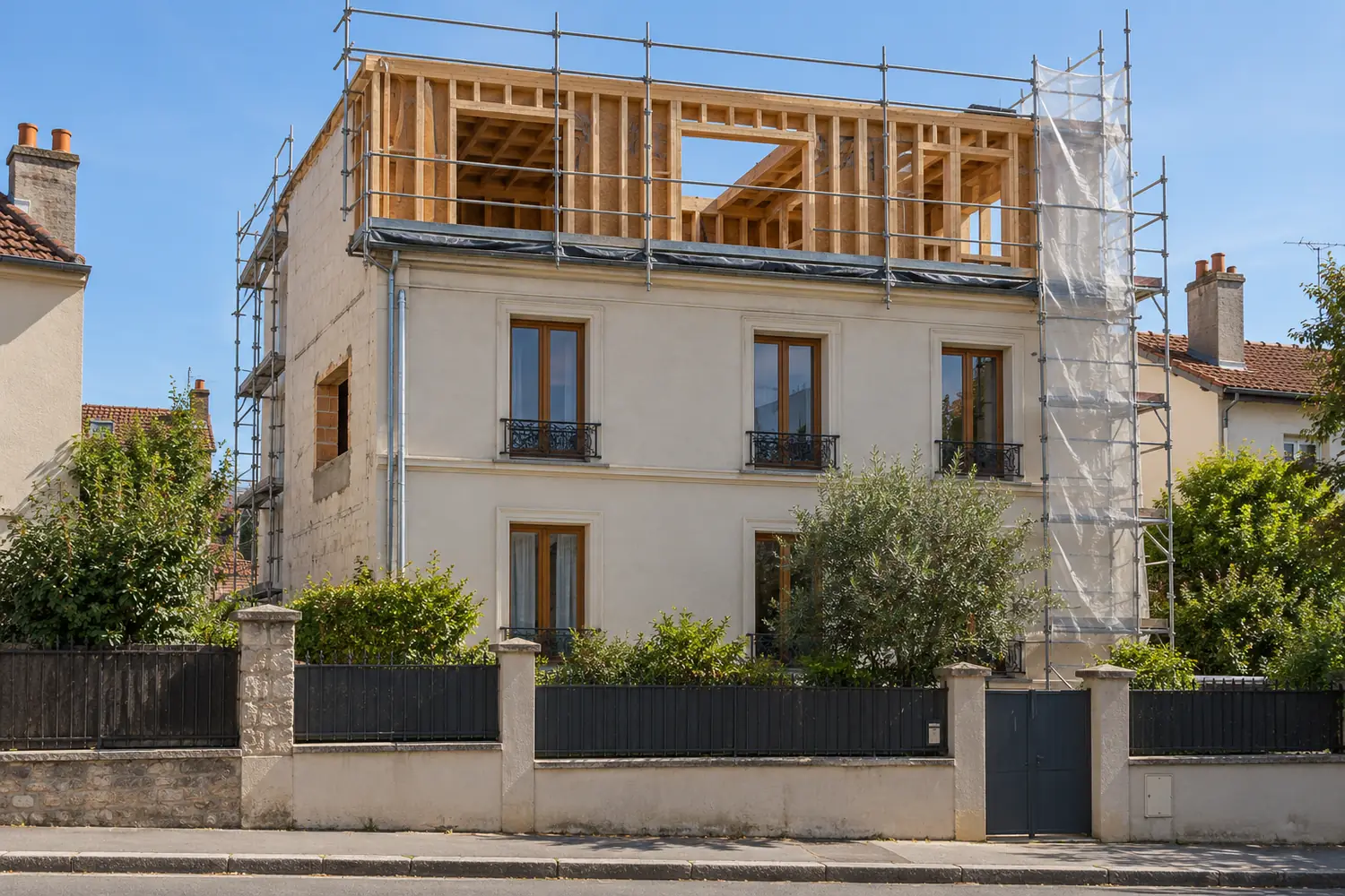 Chantier de surélévation en ossature bois sur un petit immeuble de banlieue parisienne, échafaudage et bâche, vue frontale, ciel clair