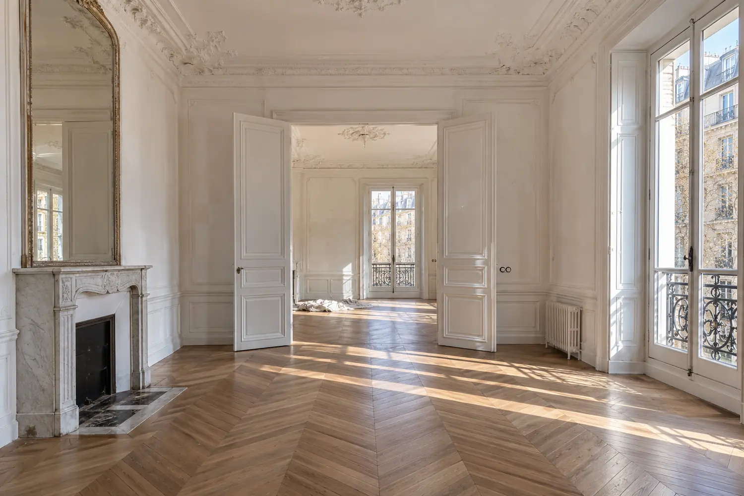 Enfilade d’un appartement haussmannien à Paris en cours de rénovation, parquet en point de Hongrie, cheminée de marbre et moulures